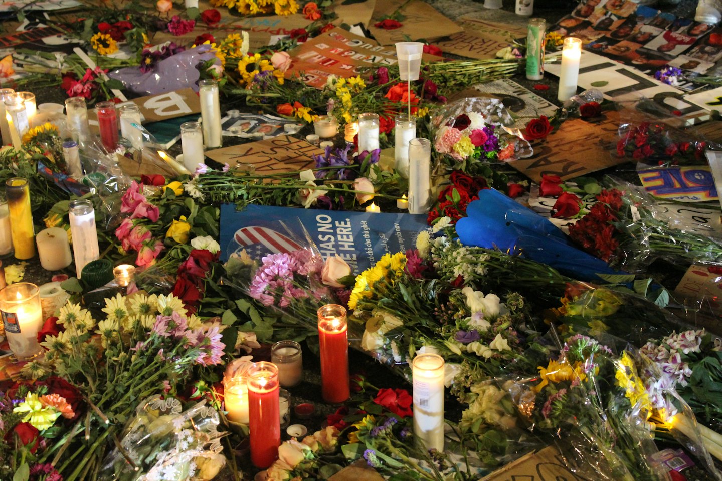 Zapaľované sviečky a kytice kvetov na pouličnom pamätníku.